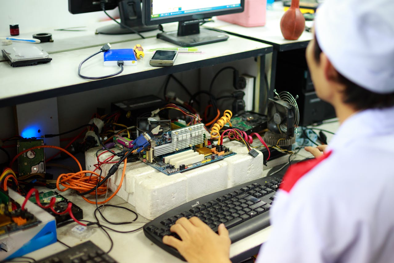 our-services-01 A man in a laboratory uniform working on computer components and wiring at a workstation.